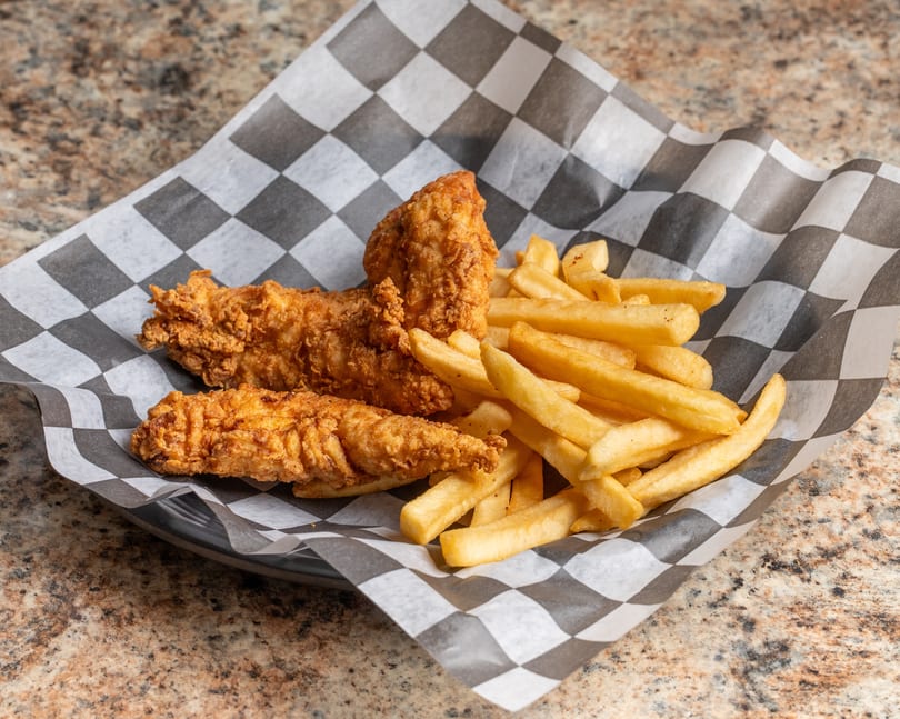 Three crispy chicken tenders and a pile of golden french fries in a checkered paper-lined basket.