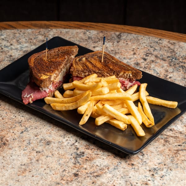 Reuben sandwich cut in half with golden french fries on a black plate.