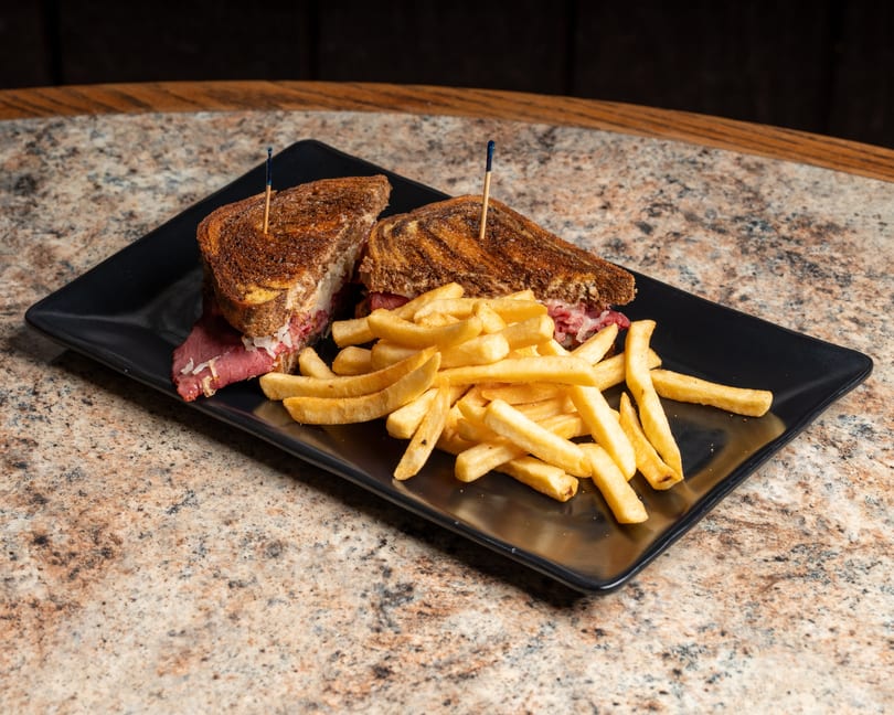 Reuben sandwich cut in half with golden french fries on a black plate.