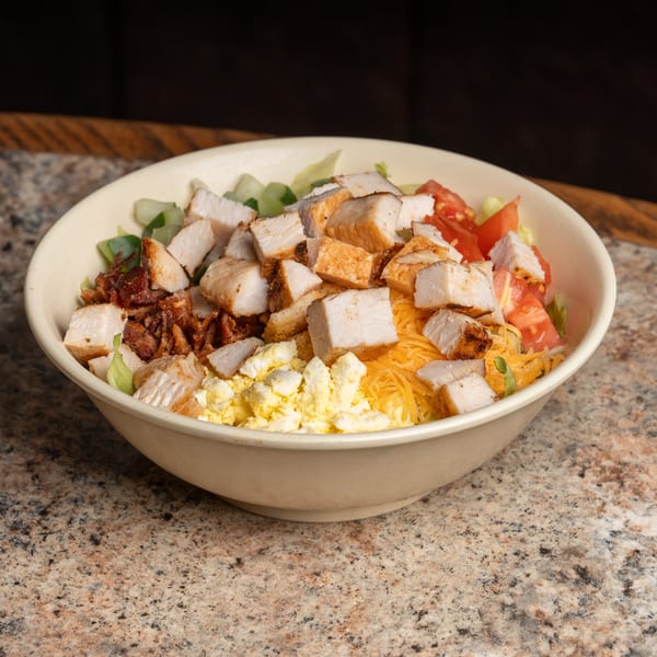 Fresh salad in a bowl with grilled chicken, bacon, shredded cheese, egg, and tomatoes.