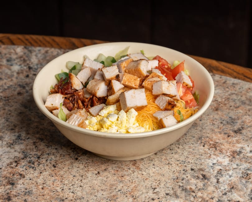 Fresh salad in a bowl with grilled chicken, bacon, shredded cheese, egg, and tomatoes.