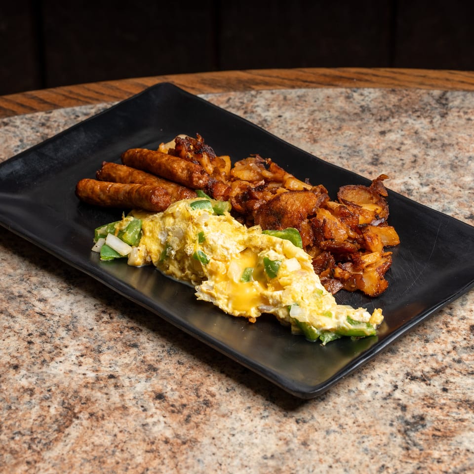 Cheesy scrambled eggs with peppers, sausages, and crispy home fries on a black plate.