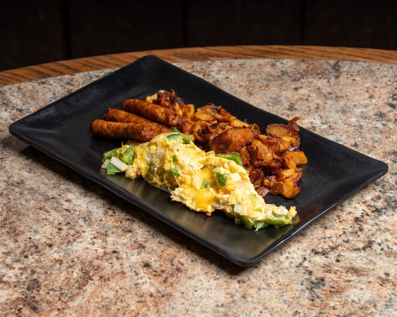 Cheesy scrambled eggs with peppers, sausages, and crispy home fries on a black plate.