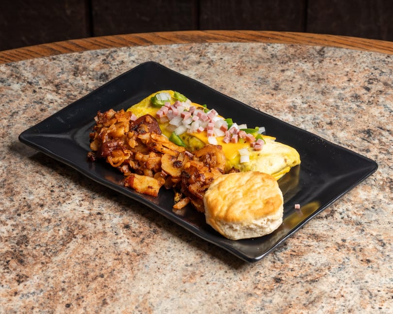 Hearty breakfast plate featuring a loaded omelet, crispy home fries, and a fluffy biscuit.