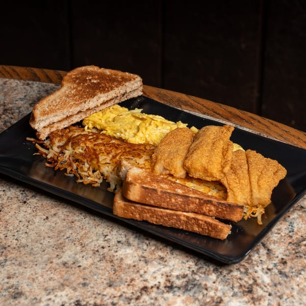 Breakfast plate with fried fish, scrambled eggs, hash browns, and toast on a black plate.