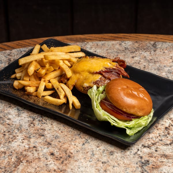 Cheesy bacon burger with lettuce, tomato, onion, and a side of seasoned fries on a black plate.